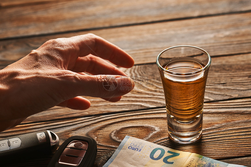 男人的手伸向乡村木桌上的杯龙舌兰酒精饮料汽车钥匙喝酒开车酗酒的安全负责的驾驶理念图片