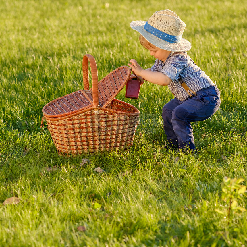 户外幼儿的肖像农村场景,岁的小男孩戴着草帽,看着野餐篮图片