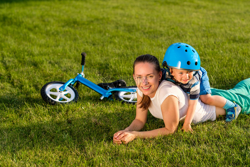 快乐的女人孩子头盔,草地上玩得很开心蓝色平衡自行车跑步自行车躺草地上家庭生活方式的场景,母亲儿子休息图片