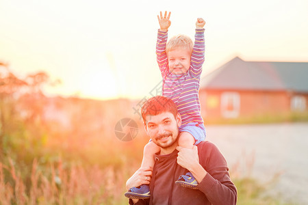 男孩背房子快乐的男人他的孩子户外玩得很开心家庭生活方式农村场景的父亲儿子夕阳的阳光下背景