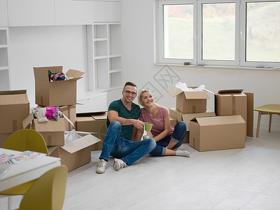 新房子里放松欢快的轻夫妇坐地板上喝咖啡,而纸板箱则躺他们周围图片
