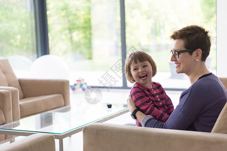 轻的母亲可爱的小女孩享受他们的空闲时间拥抱沙发上,他们豪华的家庭别墅图片