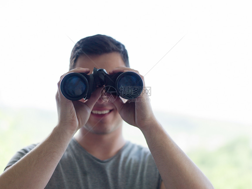 轻人站着,用望远镜透过璃窗看着远处的东西图片