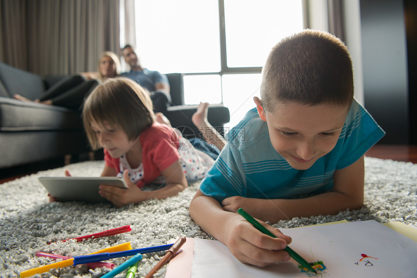 快乐的轻家庭家里玩,地板上用平板电脑儿童绘图集图片