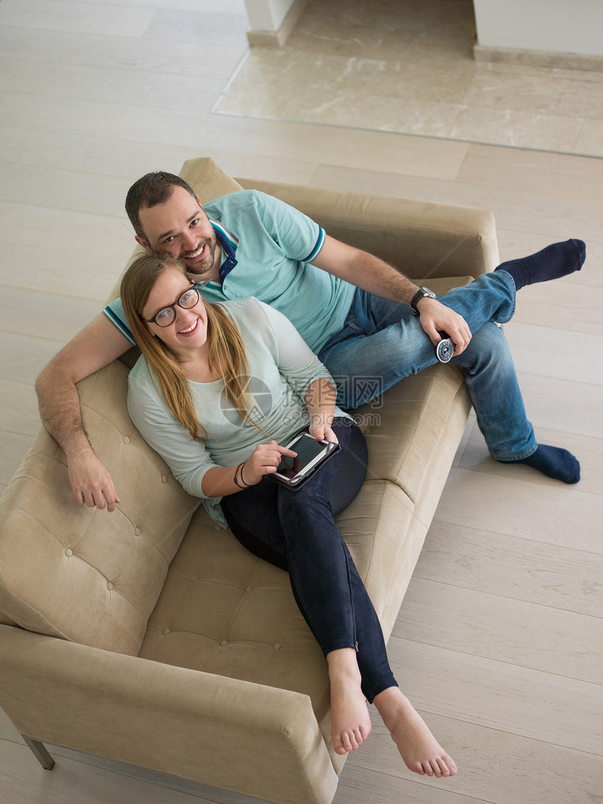 轻夫妇豪华客厅的沙发上放松,用平板电脑遥控器图片