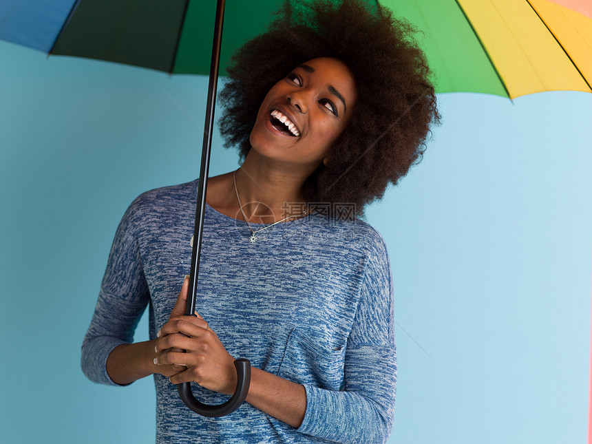 轻美丽的非裔美国妇女的肖像,着把五颜六色的伞,孤立蓝色的背景上图片