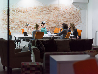 启动业务队夜间办公会议上用虚拟现实耳机,开发人员创意办公室的桌子周围与虚拟现实模拟器会背景图片