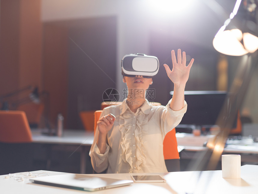 轻的女商人深夜的创业办公楼里用虚拟现实的VR耳机眼镜获得经验图片