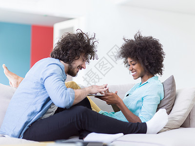 轻的多民族夫妇坐豪华客厅的沙发上,用平板电脑图片