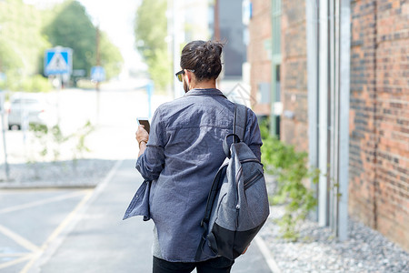 人技术旅行旅游带背包智能手机耳机的人沿着城市街道行走,听音乐图片