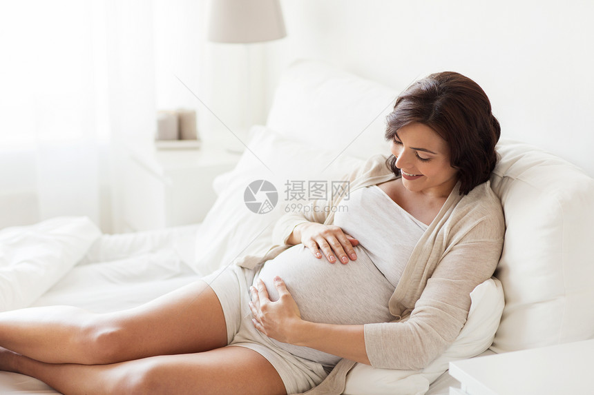 怀孕,休息,人期望的快乐的孕妇躺床上,触摸她的肚子家里图片