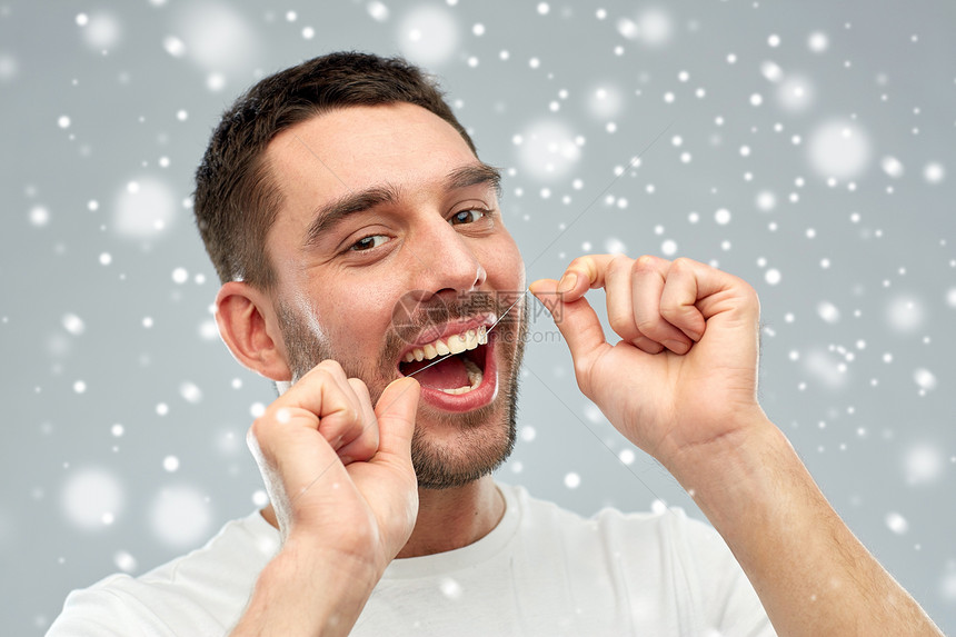 牙齿卫生,护理,人冬天的微笑的轻人用牙线清洁牙齿雪地上的灰色背景图片