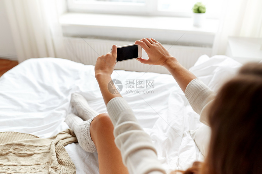 技术,冬天,增强人的轻的女人床上着智能手机,家里的卧室里用黑色的空图片