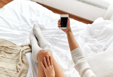 技术,冬天,增强人的轻的女人床上着智能手机,家里的卧室里黑色的空屏幕图片