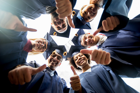 教育毕业结手势人的群快乐的国际学生穿着迫击炮板学士服站圆圈里,竖大拇指图片