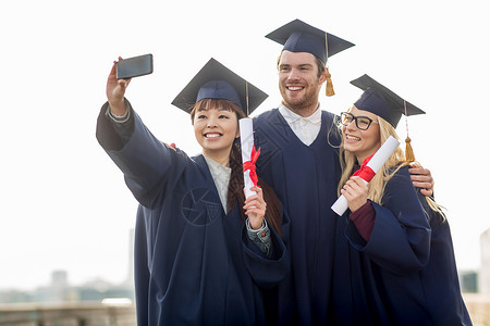 教育,毕业,技术人的群快乐的国际学生砂浆板学士学位礼服与文凭采取自拍智能手机户外背景