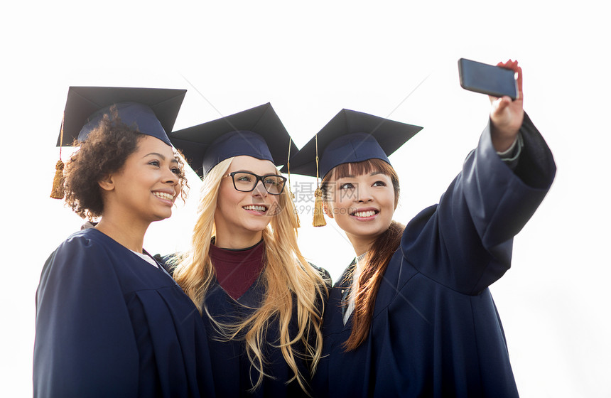 教育毕业技术人的群快乐的国际学生穿着灰浆板学士,户外用智能手机自拍图片