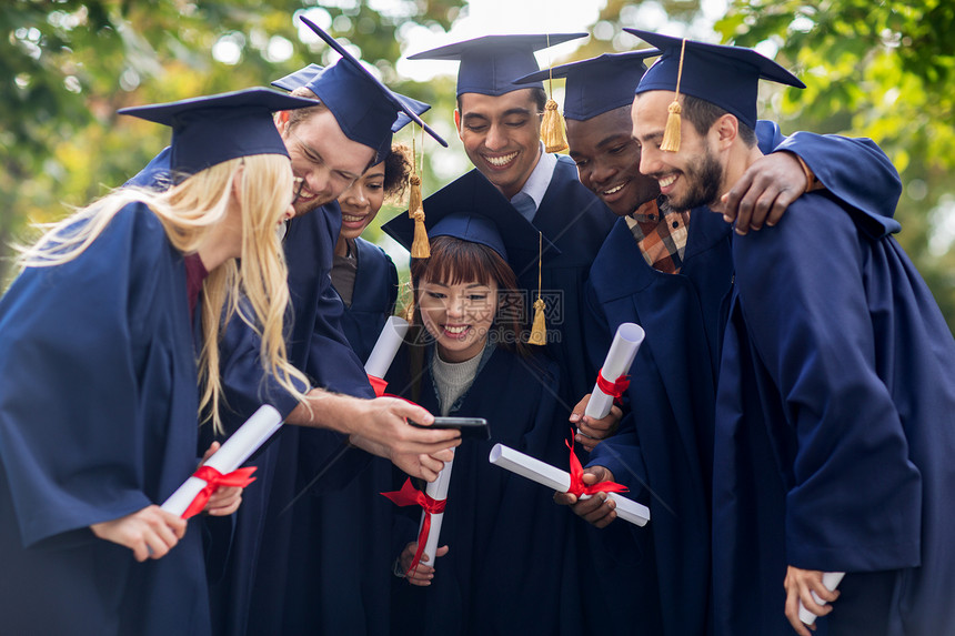 教育毕业人的群快乐的国际学生穿着灰浆板学士服,文凭智能手机图片