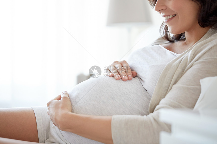 怀孕,休息,人期望的快乐微笑的孕妇躺床上,触摸她的肚子家里图片