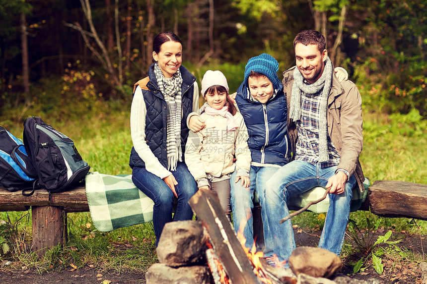 野营,旅游,徒步旅行人们的快乐的家庭坐长凳上的营地火灾树林里图片