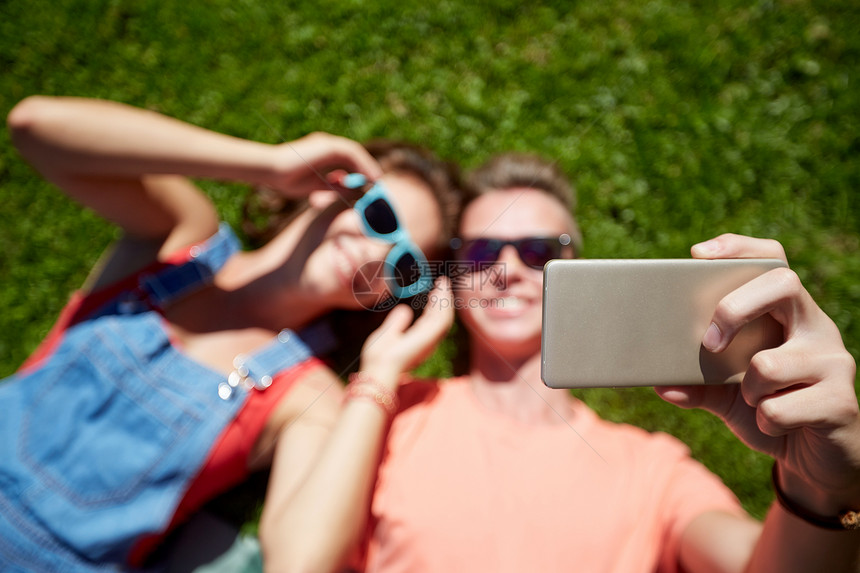 爱人的快乐的青少夫妇戴着太阳镜躺草地上,夏天智能手机上自拍快乐的夫妇夏天智能手机上自拍图片