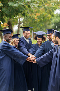 全部的幸福的教育毕业人的群快乐的国际学生穿着迫击炮板学士服,把手放背景