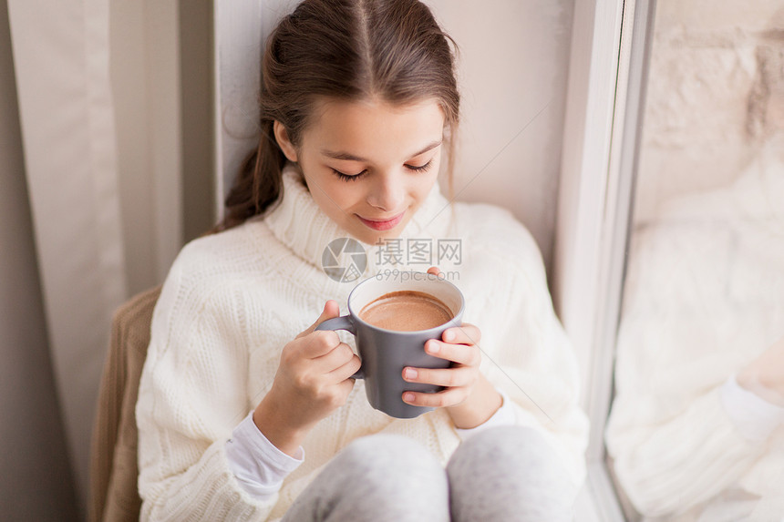 童人们的美丽的女孩与可可杯毛衣坐家里的窗户冬天可可杯的女孩坐家里的窗户上图片