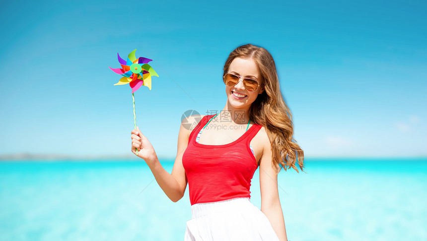 暑假,旅行,人度假的快乐的轻女人戴着太阳镜,蓝天海洋背景上戴着风车快乐的女人带着风车蓝天大海上图片