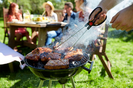 聚火盆休闲,食物,人假日的男子烹饪肉烧烤为他的朋友夏季户外聚会夏天的聚会上,男人烧烤架上煮肉背景