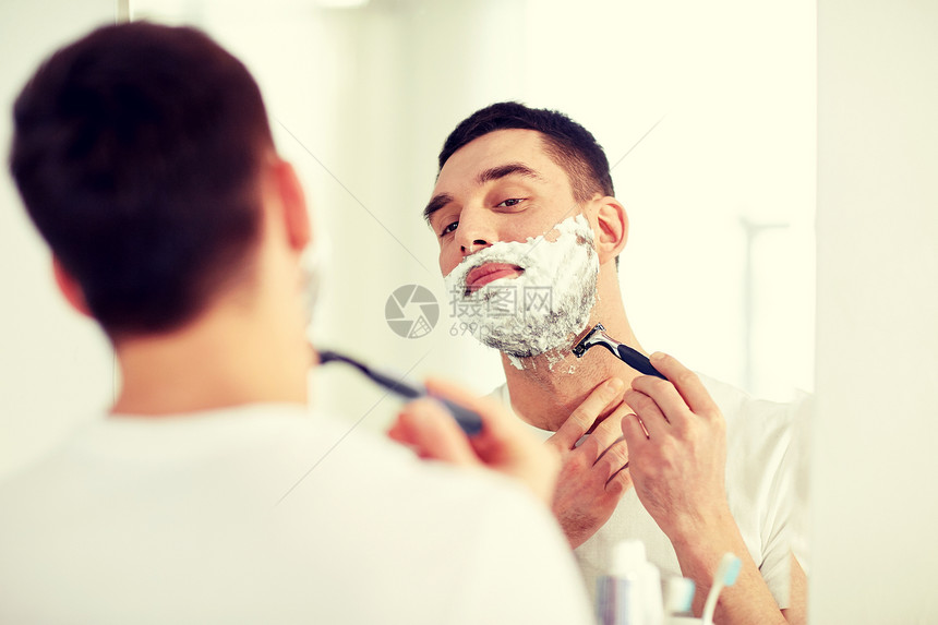 美容,卫生,剃须,美容人的轻人看着镜子剃须与手动剃须刀刀片家里浴室男人浴室用剃须刀刮胡子图片