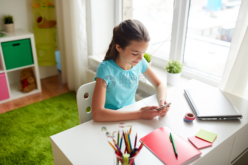 孩子,技术沟通微笑的女孩分散注意力,家庭作业短信智能手机家里智能手机的女孩分散了家庭作业的注意力图片