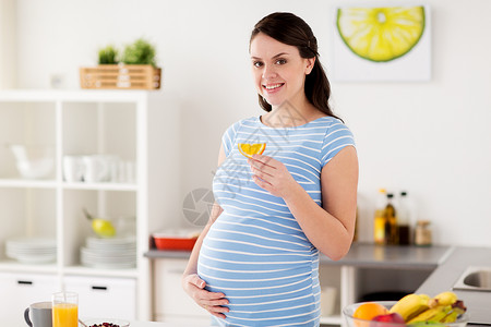 怀孕,人们健康的饮食观念快乐的孕妇家里厨房里吃橘子片快乐的孕妇家吃橘子图片