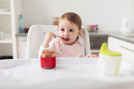 小女婴坐椅子上拿着勺子吃罐子里的食物背景图片