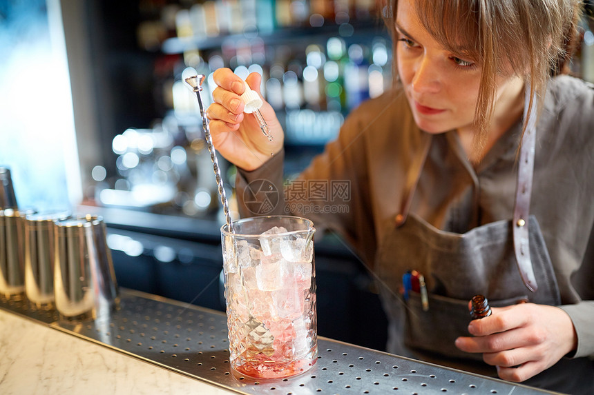 酒精饮料,人豪华女调酒师准备鸡尾酒,并酒吧柜台用冰块将香精加入璃杯中酒保酒吧的鸡尾酒杯中加入香精图片