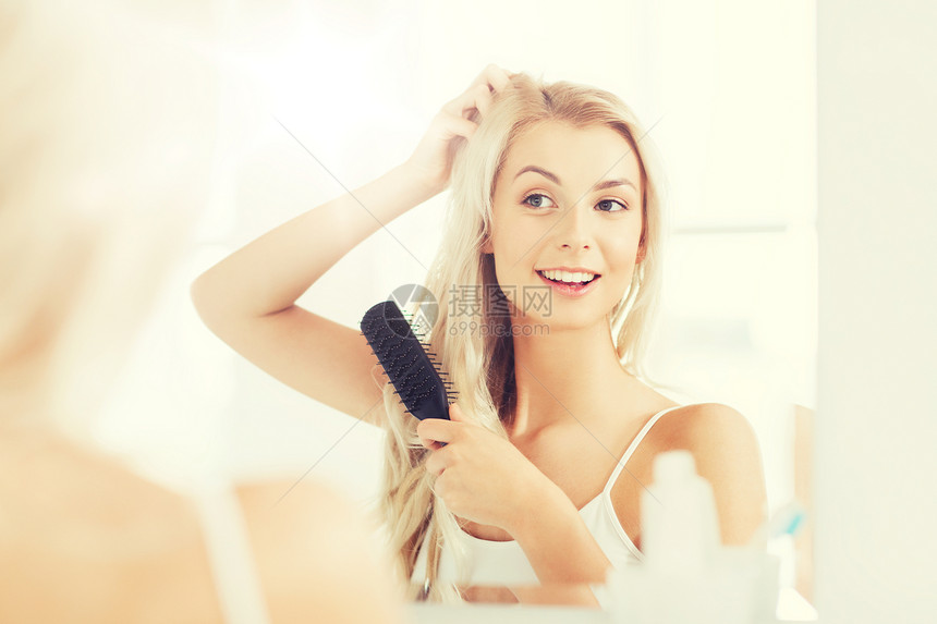 美丽,修饰人的微笑的轻女人看着镜子,家里的浴室用梳子梳头快乐的女人浴室用梳子刷头发快乐的女人浴室用梳子刷图片
