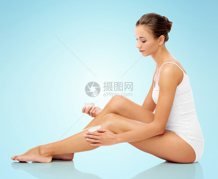 人,身体护理美容美丽的女人她的腿上涂上保湿霜的蓝色背景女人腿上涂保湿霜女人腿上涂保湿霜图片