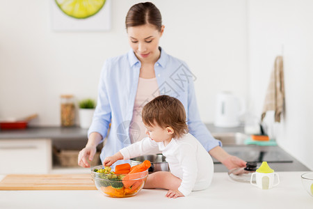家庭,食物,健康的饮食,烹饪人们的快乐的母亲小女婴家里厨房里吃碗蔬菜快乐的母亲婴儿家里的厨房里吃食物快乐背景图片