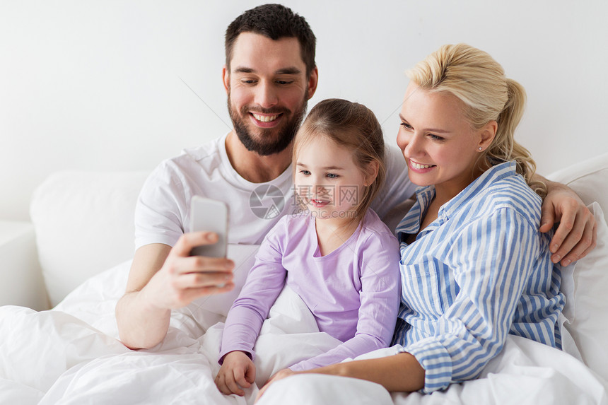 人,家庭技术的快乐的母亲,父亲小女孩家里用智能手机自拍幸福的家庭家里用智能手机自拍图片