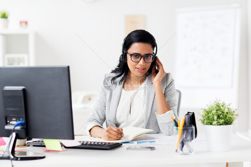 沟通,商业,人技术微笑的女商人帮助热线接线员与耳机电脑交谈写作笔记本办公室办公室带耳机笔记本的女商人图片