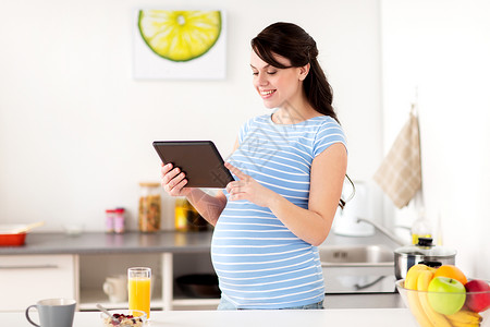 健康饮食,怀孕人的孕妇与平板电脑家里厨房吃早餐孕妇家里吃平板电脑图片