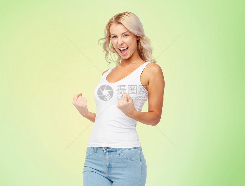手势,表情人的快乐的微笑轻女子穿着白色上衣牛仔裤拳头泵绿色背景快乐的轻女人拳头泵的手势图片