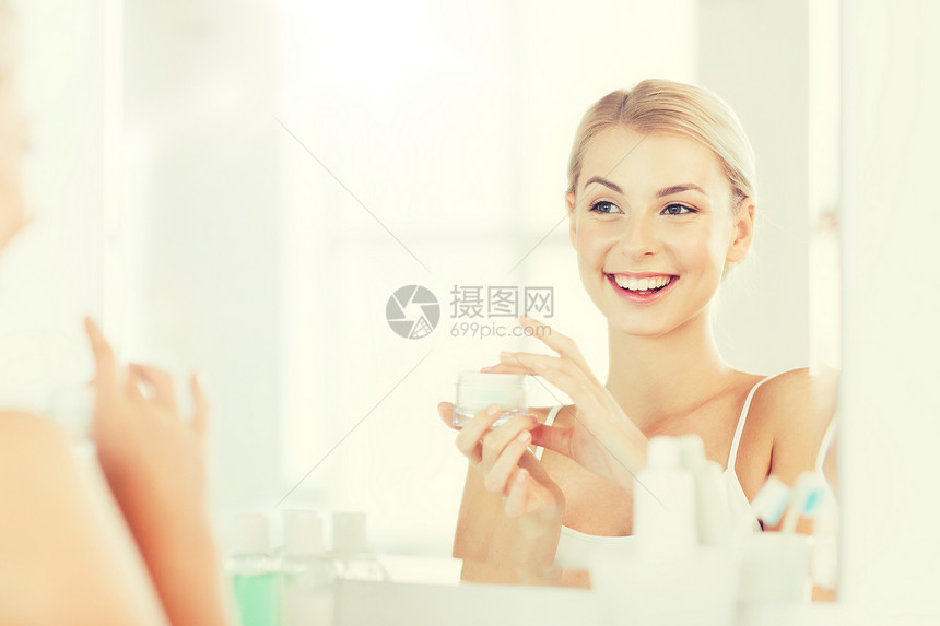 美丽,皮肤护理人的微笑的轻妇女应用奶油镜子家里的浴室快乐的女人浴室用奶油洗脸图片