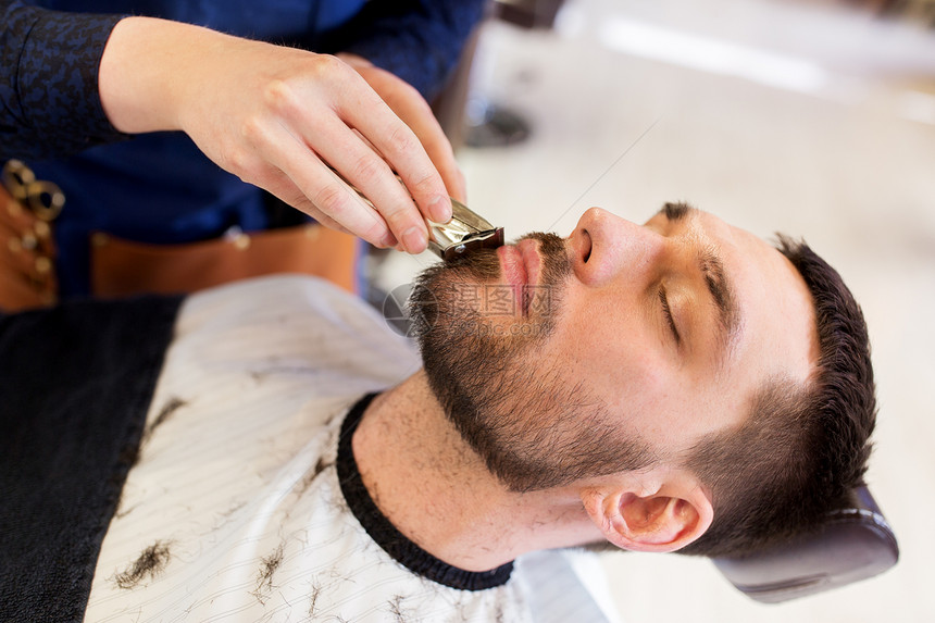 美容人的男人理发师与修剪剃须刀切割胡须理发店男人理发师沙龙剪胡子图片
