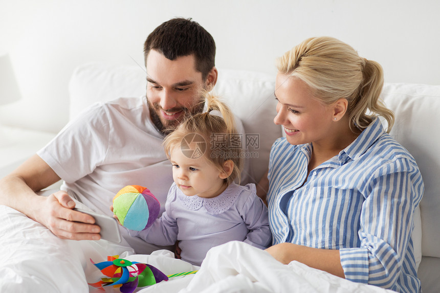 人,家庭技术的快乐的母亲,父亲小女孩家里的床上智能手机家里智能手机的幸福家庭图片