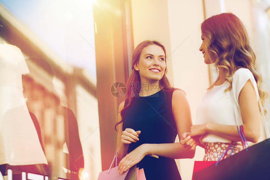 销售,消费主义人们的快乐的轻妇女带着购物袋城市的商店窗口交谈快乐的女人商店橱窗里着购物袋图片