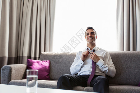 人休息的快乐的微笑商人酒店房间摘下他的领带快乐的商人旅馆房间脱下领带图片