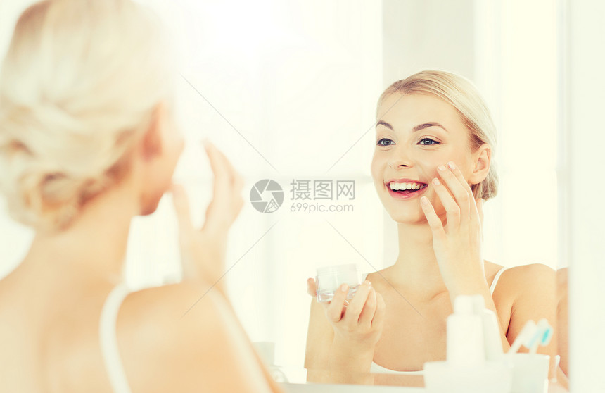 美丽,皮肤护理人的微笑的轻妇女应用奶油镜子家里的浴室快乐的女人浴室用奶油洗脸图片