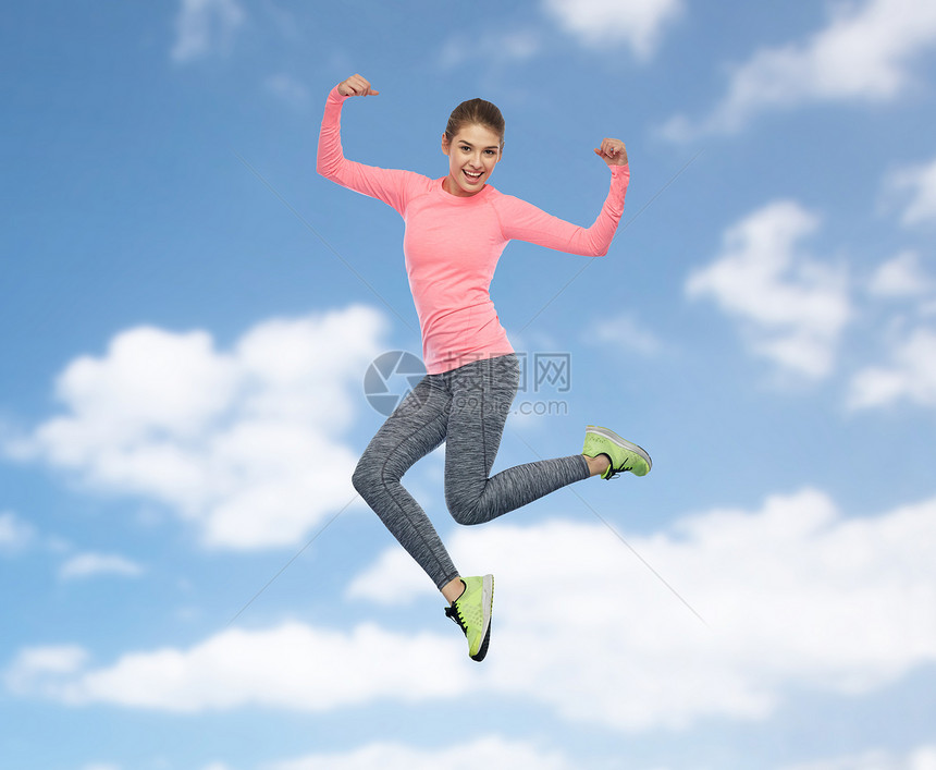 运动,健身,运动人的快乐的微笑轻女子空中跳跃,并蓝天云层背景上力量姿态快乐微笑运动的轻女人天空中跳跃图片