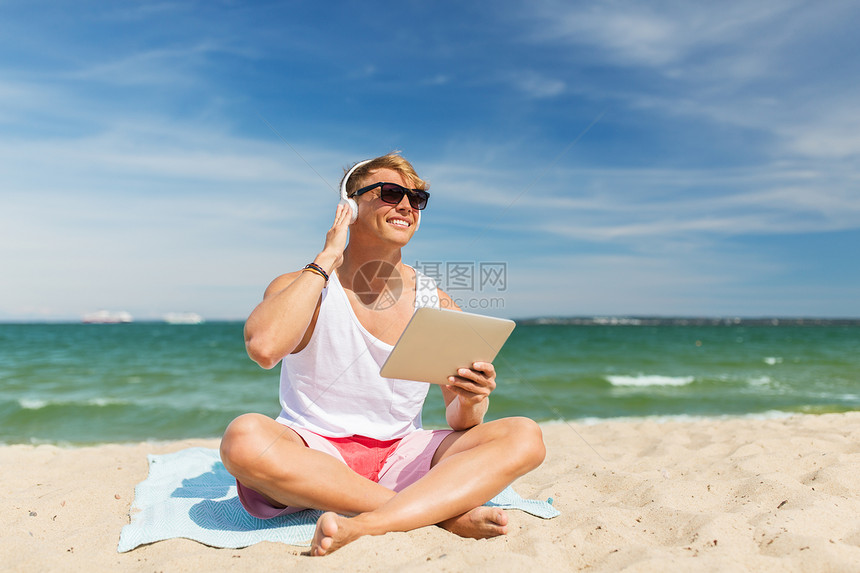 暑假,技术人的快乐的微笑轻人与平板电脑耳机,听音乐日光浴海滩毛巾快乐的人与平板电脑耳机海滩上图片