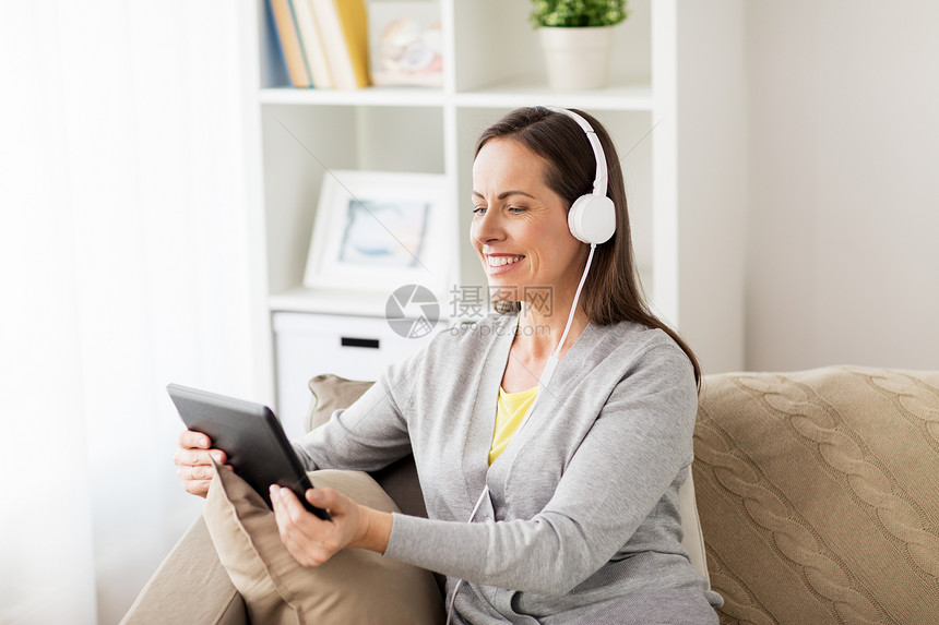 人技术休闲理念快乐的女人坐沙发上,用平板电脑耳机家听音乐家里平板电脑耳机的快乐女人图片
